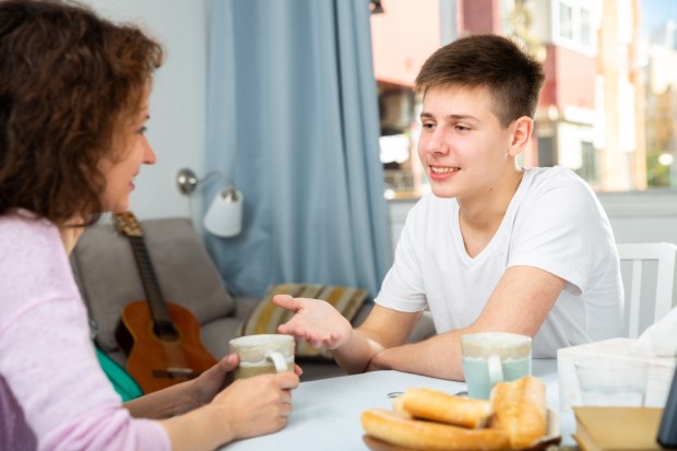 Portrait of happy teenager having friendly chat with his mom at home